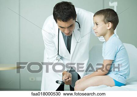 Stock Image - Doctor checking boy's reflexes with reflex hammer. Fotosearch