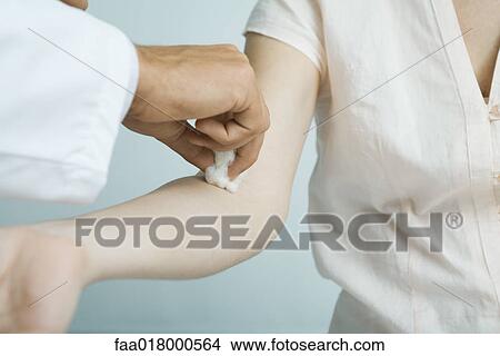 Doctor cleaning woman's arm with cotton ball View Large Photo Image Picture - Doctor cleaning woman's arm with cotton ball. Fotosearch