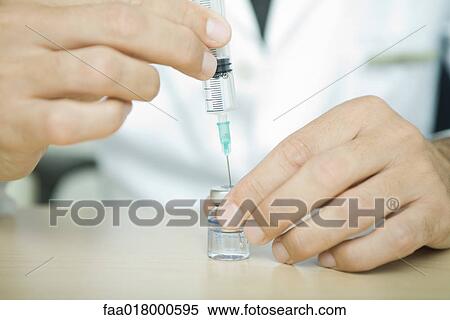 Stock Photography - Doctor filling syringe from bottle. Fotosearch