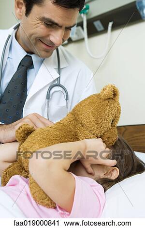 Stock Image - Doctor holding teddy bear up to sick child's face. Fotosearch