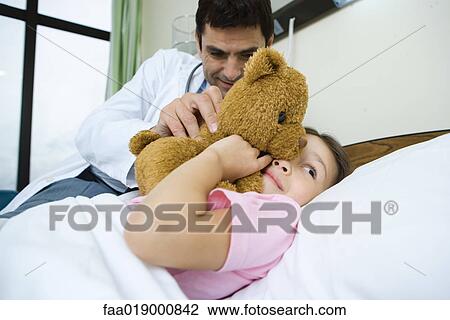 Stock Image - Doctor holding teddy bear up to sick child's face. Fotosearch