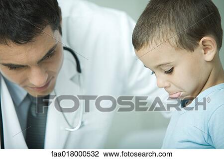 Stock Image - Doctor leaning over boy, boy making face. Fotosearch