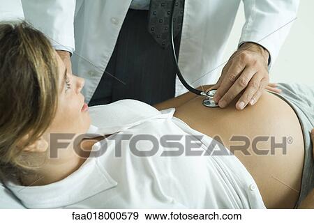 Stock Photo - Doctor listening to pregnant woman's stomach with stethoscope. Fotosearch