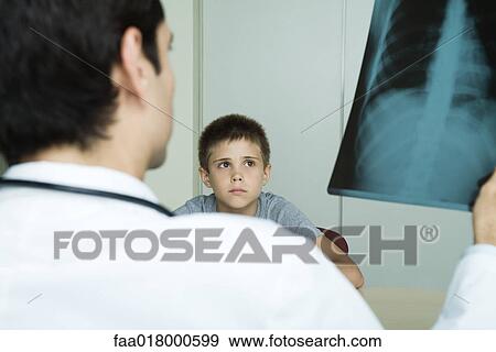 Doctor sitting across from boy, holding up x-ray View Large Photo Image Stock Photo - Doctor sitting across from boy, holding up x-ray. Fotosearch