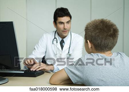 Stock Photo - Doctor sitting across from boy, using computer. Fotosearch
