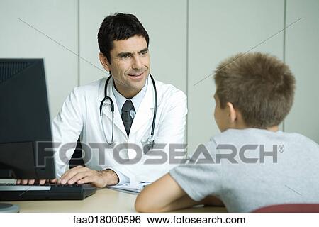 Stock Photograph - Doctor sitting across from boy, using computer, smiling at boy. Fotosearch