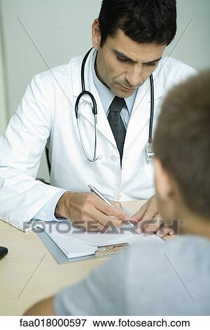 Stock Photo - Doctor sitting across from boy, writing on clipboard. Fotosearch