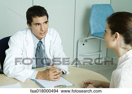 Doctor sitting across from female patient View Large Photo Image Picture - Doctor sitting across from female patient. Fotosearch