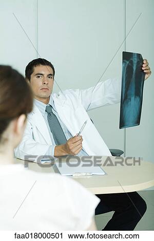 Stock Image - Doctor sitting across from female patient, holding up x-ray. Fotosearch