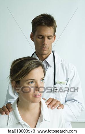Stock Image - Doctor standing behind woman, hands on her shoulders. Fotosearch