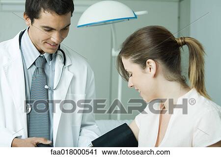 Stock Image - Doctor taking woman's blood pressure. Fotosearch