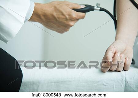 Stock Photo - Doctor taking woman's blood pressure, close-up. Fotosearch