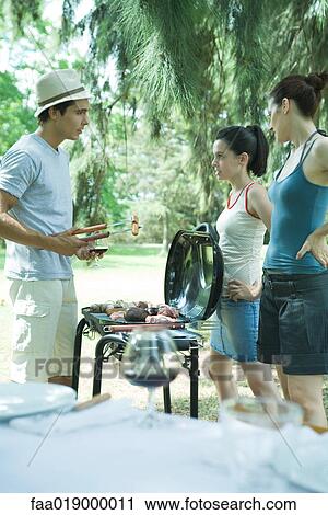 Stock Image - Family grilling meat on barbecue. Fotosearch