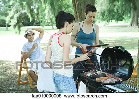 Family grilling meat on barbecue View Large Photo Image Stock Photo - Family grilling meat on barbecue. Fotosearch