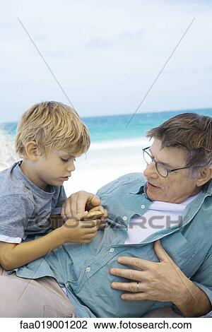 Stock Image - Family having picnic on beach, boy talking to grandfather. Fotosearch
