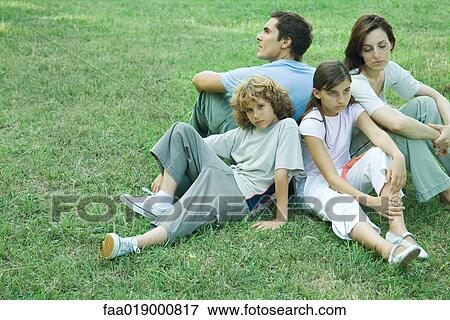 Stock Photo - Family outdoors, sitting on grass back to back. Fotosearch