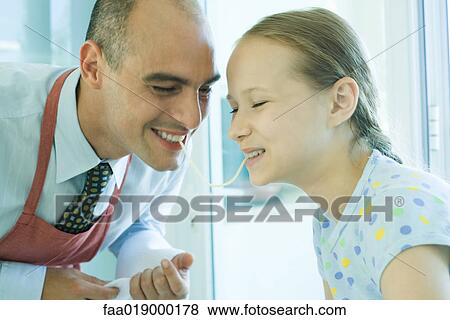 Stock Photo - Father and daughter sharing spaghetti noodle, laughing. Fotosearch