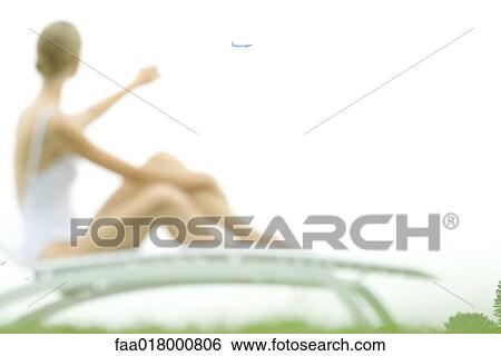 Female figure sitting on lounge chair, pointing to airplane in distance, defocused View Large Photo Image Stock Photograph - Female figure sitting on lounge chair, pointing to airplane in distance, defocused. Fotosearch