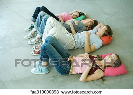 Stock Image - Four teen friends lying on backs on floor with knees up. Fotosearch