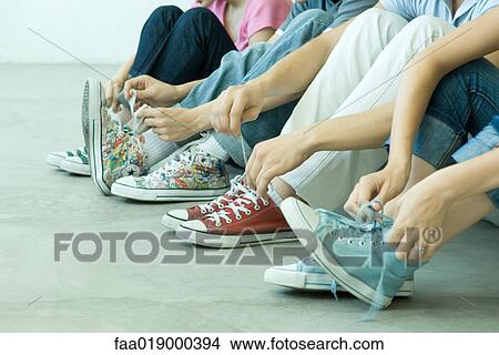Picture - Four teen friends tying laces, all wearing canvas shoes. Fotosearch