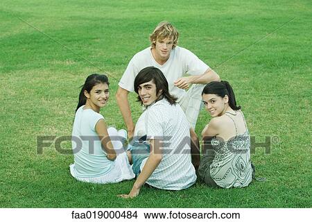 Picture - Four young friends sitting on grass, looking at camera. Fotosearch