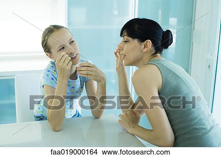 Picture - Girl eating ice cream dessert, woman leaning toward girl enviously. Fotosearch