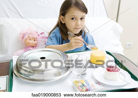 Stock Image - Girl eating meal in hospital bed. Fotosearch