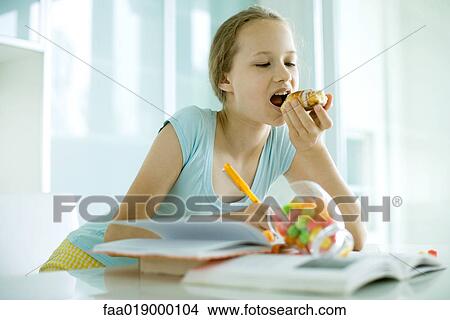 Picture - Girl eating sweet snacks and doing homework. Fotosearch