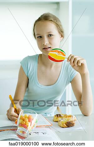 Stock Image - Girl eating sweets and doing homework. Fotosearch