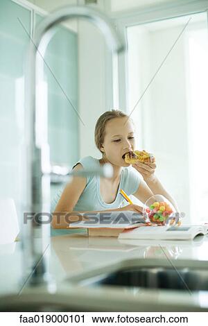 Stock Image - Girl eating sweets and doing homework. Fotosearch
