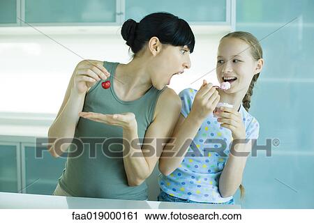 Girl holding ice cream dessert, next to woman holding cherry, woman leaning toward girl with mouth wide open View Large Photo Image Stock Image - Girl holding ice cream dessert, next to woman holding cherry, woman leaning toward girl with mouth wide open. Fotosearch