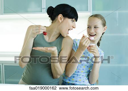 Girl holding ice cream dessert, next to woman holding cherry, woman leaning toward girl with mouth wide open View Large Photo Image Stock Image - Girl holding ice cream dessert, next to woman holding cherry, woman leaning toward girl with mouth wide open. Fotosearch