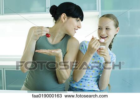 Girl holding ice cream dessert, next to woman holding cherry, woman leaning toward girl View Large Photo Image Stock Image - Girl holding ice cream dessert, next to woman holding cherry, woman leaning toward girl. Fotosearch