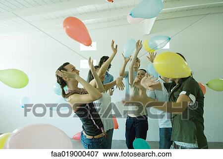 Stock Photo - Group of young friends hitting balloons floating in the air. Fotosearch