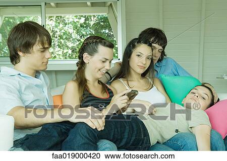 Stock Image - Group of young friends sitting on sofa, one lying across legs of others. Fotosearch