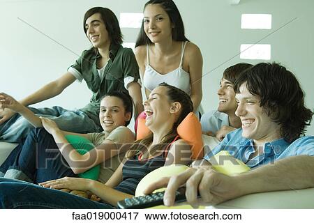Stock Photo - Group of young friends sitting on sofa, watching TV. Fotosearch