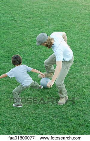 Stock Image - Man and boy playing soccer on grass, high angle view, full length. Fotosearch