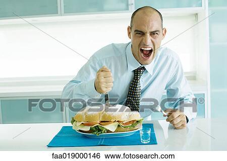 Man cutting into large sandwich with knife and fork, making face View Large Photo Image Stock Photograph - Man cutting into large sandwich with knife and fork, making face. Fotosearch