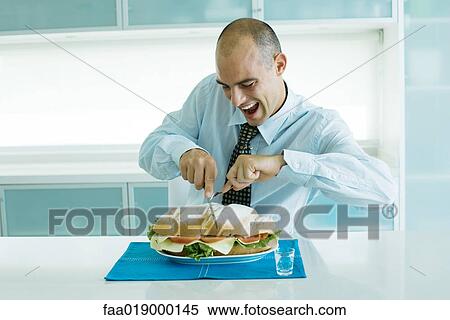 Stock Photography - Man cutting into large sandwich with knife and fork. Fotosearch