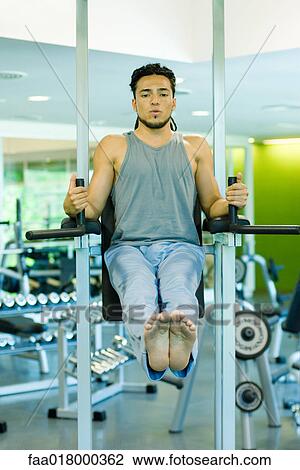 Stock Image - Man doing leg lifts with exercise machine. Fotosearch