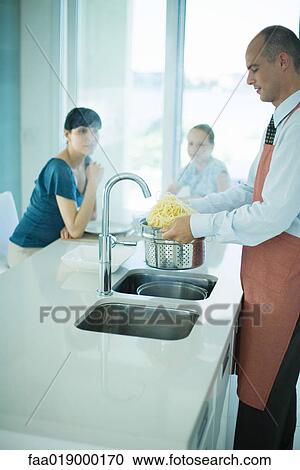Man draining spaghetti over kitchen sink while wife and daughter watch View Large Photo Image Stock Image - Man draining spaghetti over kitchen sink while wife and daughter watch. Fotosearch
