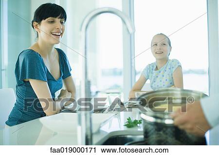 Stock Image - Man draining spaghetti over kitchen sink while wife and daughter watch. Fotosearch