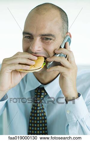 Man eating hamburger and using cell phone View Large Photo Image Stock Image - Man eating hamburger and using cell phone. Fotosearch