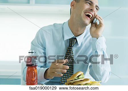 Stock Photo - Man eating junk food and using cell phone. Fotosearch