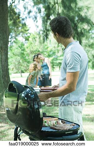 Man grilling meat on barbecue, family whispering in background View Large Photo Image Stock Photography - Man grilling meat on barbecue, family whispering in background. Fotosearch