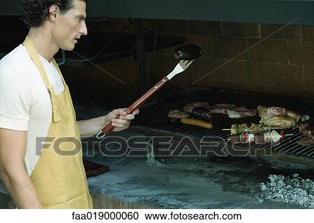 Man grilling meat on barbecue View Large Photo Image Stock Image - Man grilling meat on barbecue. Fotosearch