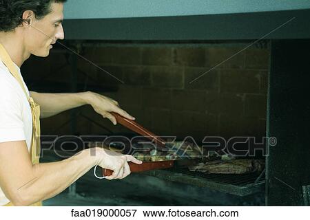 Stock Photo - Man grilling meat on barbecue. Fotosearch