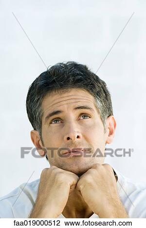 Stock Image - Man, hands under chin, looking up, portrait. Fotosearch