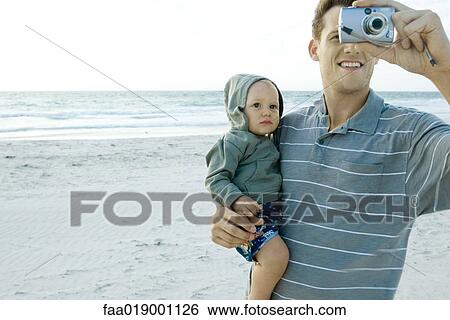 Man holding baby and using camera on beach View Large Photo Image Stock Photograph - Man holding baby and using camera on beach. Fotosearch
