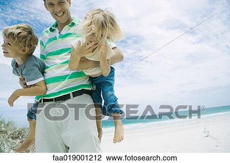 Stock Image - Man holding children under his arms on beach. Fotosearch